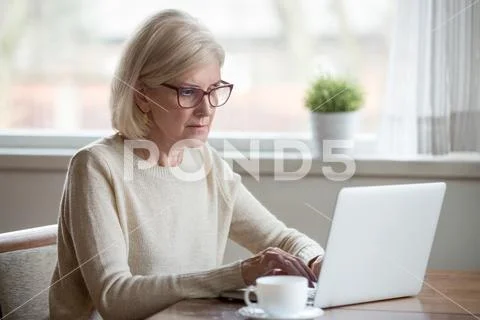 Serious mature middle aged business woman using laptop typing em Stock Photos