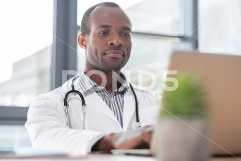 Serious medical worker looking at his laptop Stock Photos