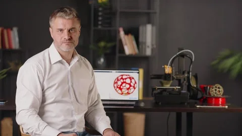A serious middle aged man graphic designer sits sideways by the table. A Stock Footage 259497121