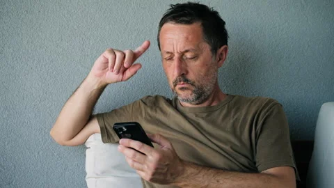 Serious, middle-aged man stares at his smartphone with a pensive expression.. Vídeo Stock 346808709