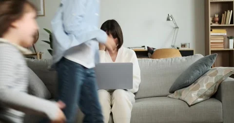Serious Mother Working on Laptop While Children Play Around Video stock 254442224