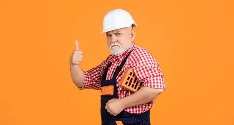 Serious old aged man bricklayer in helmet on yellow background Stock Photos