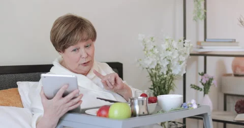 Serious old lady in rob talking during video call while having breakfast in bed Stock Footage 135589679