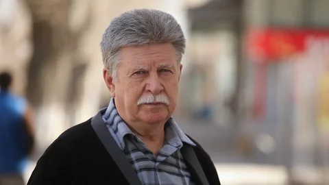 A serious old man with mustache puts on glasses and stands on an alley in spring Stock-Footage 88449607