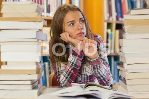 Serious pretty student sitting between piles of books Stock Photos