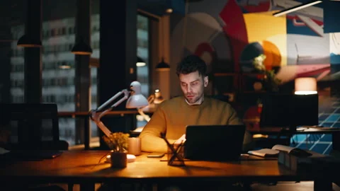 Serious programmer focused laptop sitting in lamp light night office closeup. Stock Footage 340114221