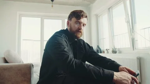 Serious redhead man with beard sitting at home and looking at camera. 스톡 동영상 174717231