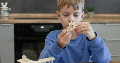 Serious schoolboy assembles airplane part modelling at desk Stock Footage 323973462