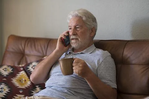 Serious senior aged man doing phone call sitting at home with smart phone - s Stock Photos