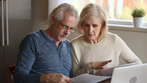 Serious senior mature couple disputing holding paper bills checking finances Stock Footage