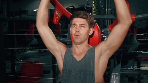 Serious sporty man doing exercise in gym in dark light alone. Pretty brunette 库存影片 251906353