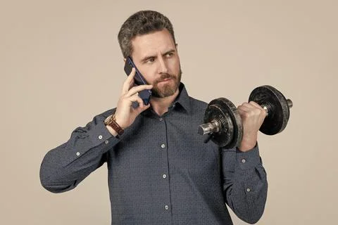 Serious strong bearded man businessman training with barbell and speaking on Stock Photos