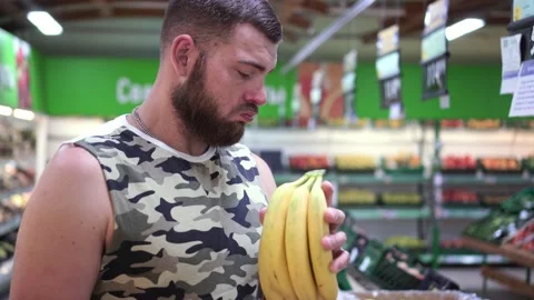 Serious strong man with a beard picks bananas at the grocery supermarket Stock Footage 141262173