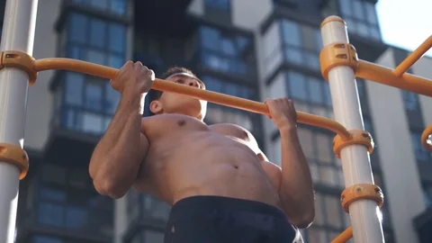 Serious strong young man in looking straight while doing pull-ups on workout Stock Footage 112951033