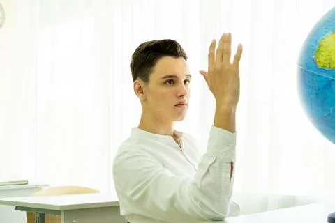A serious student giving an answer in class with his hand raised is sitting at a 写真素材