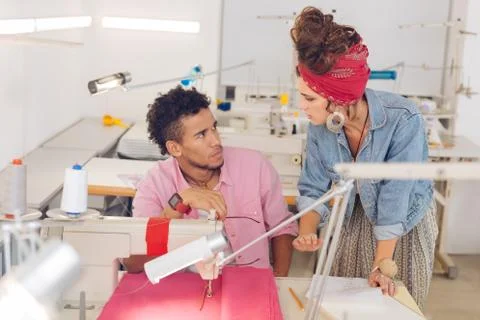 Serious tailor looking at his experienced colleague and listening to her Stock Photos