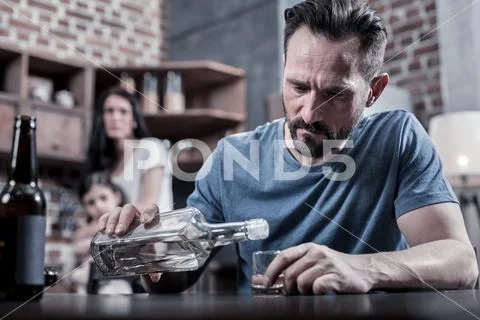 Serious unhappy man pouring vodka into his glass Stock Photos
