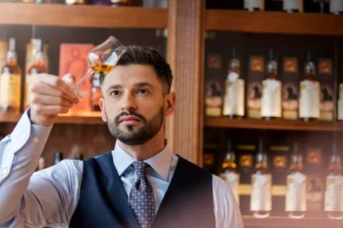 Serious well-dressed bartender examining whiskey Stock Photos