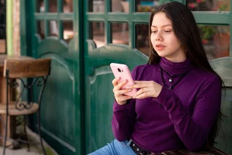 Serious woman sitting while using her smart phone in urban street. Stock Photos