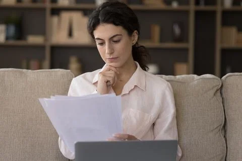 Serious woman working with correspondence seated on sofa with laptop Stock Photos