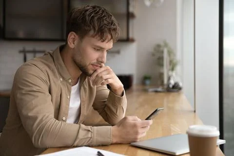 Serious young 30s man sit indoor with smartphone Stock Photos