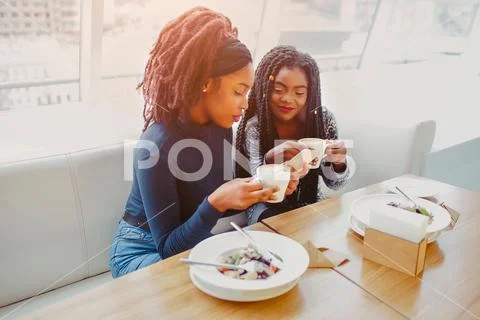 Serious young african women sit in cafe. They hold cup of coffee and phone Stock Photos