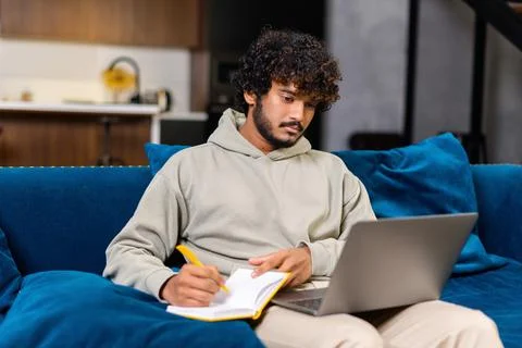 Serious young curly man using laptop computer for studying and work on the 写真素材
