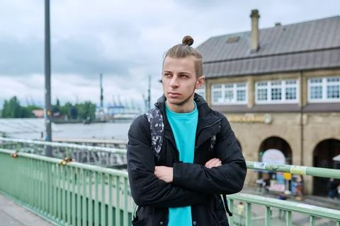 Serious young guy in jacket with backpack with crossed arms outdoor, city Stock Photos
