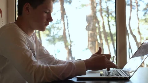 A serious Young guy is typing on a laptop in a cafe near the window,drinks water Stock Footage 114117474