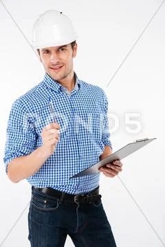 Serious young man builder in hard hat writing on clipboard Stock Photos