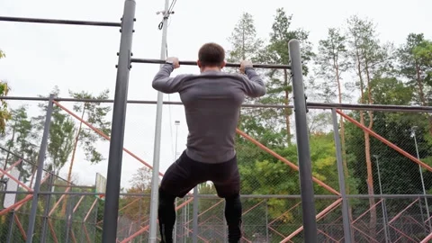 Serious young man doing pull ups on sports ground Stock Footage 257821468