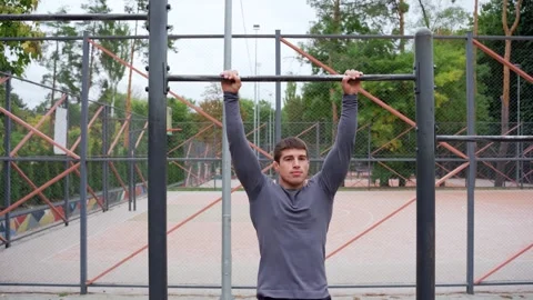 Serious young man doing pull ups on sports ground Stock Footage 265399840