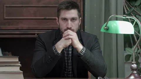 Serious young man sitting at the study table with books and looking into the Stock-Footage 73687817