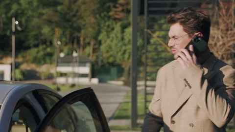 Serious young man talking on a mobile phone sitting in a car in the sunlight Stock Footage 252142407