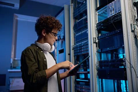 Serious young man working in data center standing at open server rack cabinet Stock Photos
