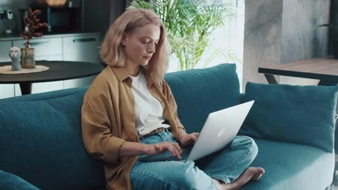 Serious young woman sitting on couch using laptop notebook typing message Video stock 143592853
