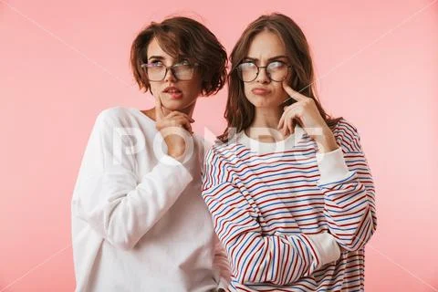 Serious young women friends posing isolated over pink background. Stock Photos