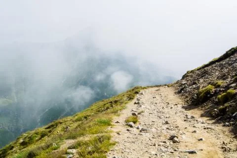 A serpentine path going down in the Carpatian mountains and a big fog cloud a Stock Photos