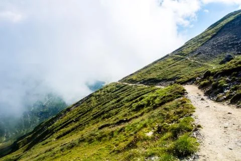 A serpentine path going down in the Carpatian mountains and a big fog cloud a Stock Photos