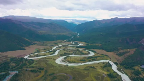 Serpentine river carving through meadows, forest and mountain terrain Stock Footage 302270164