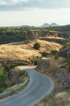 Serpentine road surrounded by pine trees and two mountain peaks in the distan Stock Photos
