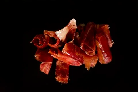 Serrano ham cut on black background. Stock Photos