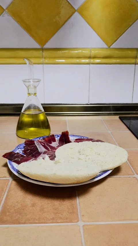 Serrano ham, hot bread and olive oil in a Spanish kitchen Stock Footage 297067603