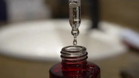 Serum drop falling from glass dropper into a red bottle close-up Video stock 333809684