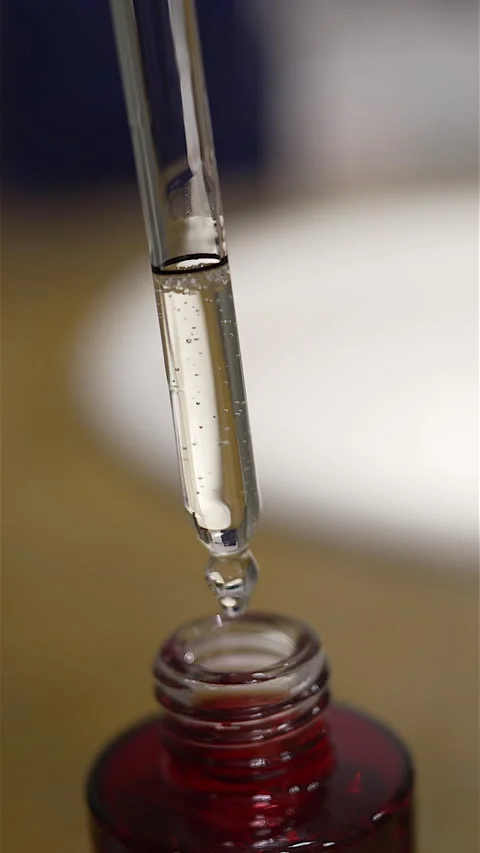 Serum drop falling from glass dropper into a red bottle Video stock 333810728