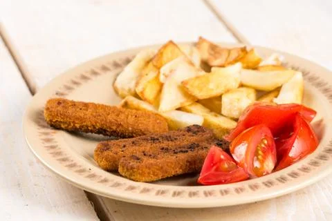 Served meal on the table, fried fish meat sticks with potatoes and tomato sal Stock Photos