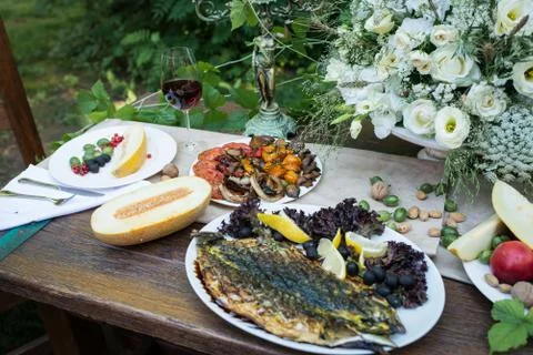 Served table with grilled vegetables and fish, glass of red wine and fruits Stock Photos