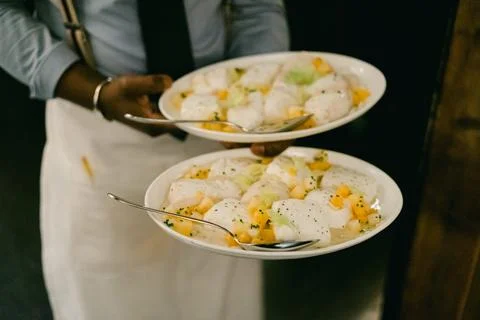 Server carries two plates of fresh fish dishes with garnishes in a busy Stock Photos