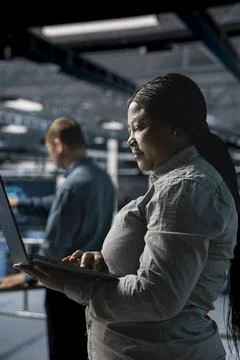 Server farm colleagues running diagnostics on infrastructure using laptop Stock Photos