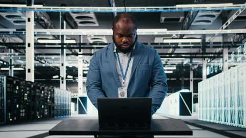 Server farm programmer at workplace desk using laptop to optimize electronics Video stock 330378638